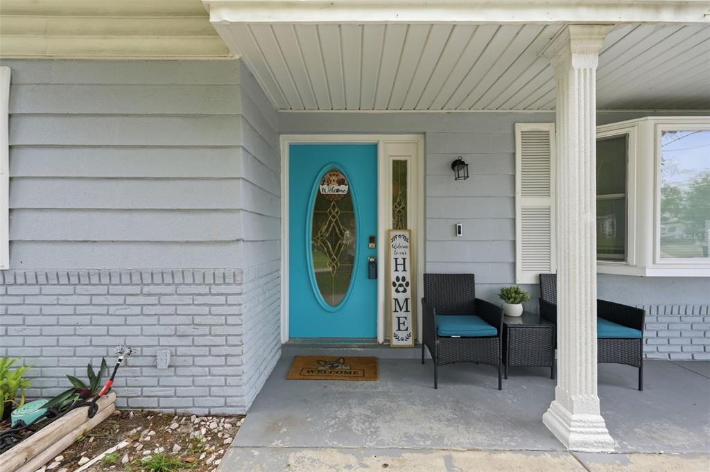 A front porch features a bright blue door, two wicker chairs, and gray siding — 4344 OAK BLUFF AVENUE, HOLIDAY, FL