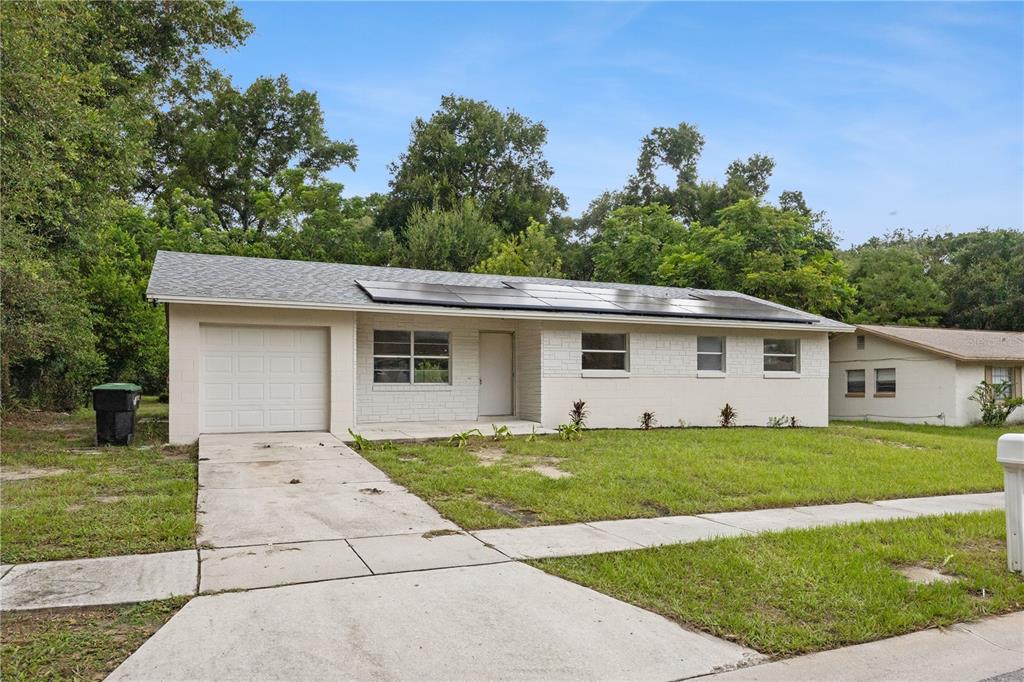 A single-story house with a concrete driveway, white brick exterior, and solar panels on the roof — 3688 RUNDO DRIVE, ORLANDO, FL