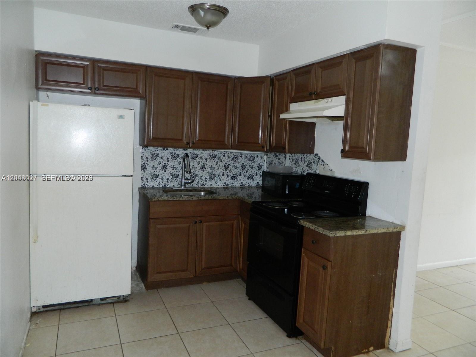 A kitchen features dark wood cabinets, a white refrigerator, black appliances, and floral backsplash tile — 1890 NW 58th Ter # 2, Sunrise FL 33313, SUNRISE, FL