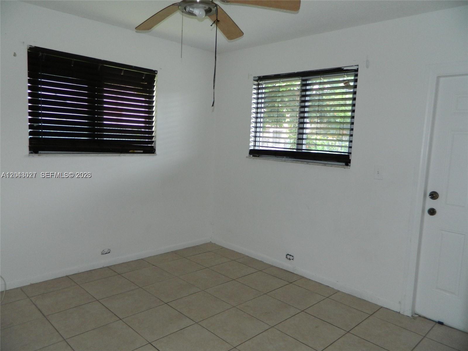An empty room features white walls, tan tile flooring, a ceiling fan, and two windows — 1890 NW 58th Ter # 2, Sunrise FL 33313, SUNRISE, FL