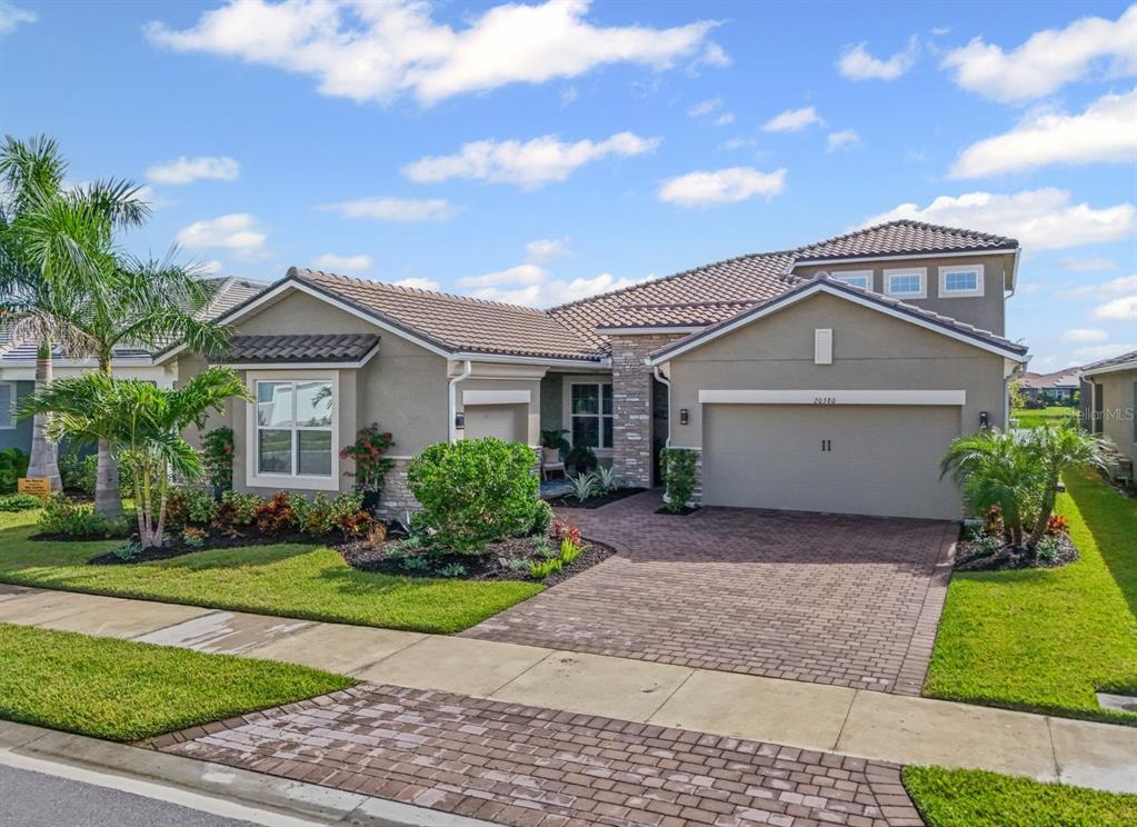 A single-story house with a beige stucco exterior, stone accents, and a brick paver driveway — 20380 SYMPHONY PLACE, VENICE, FL