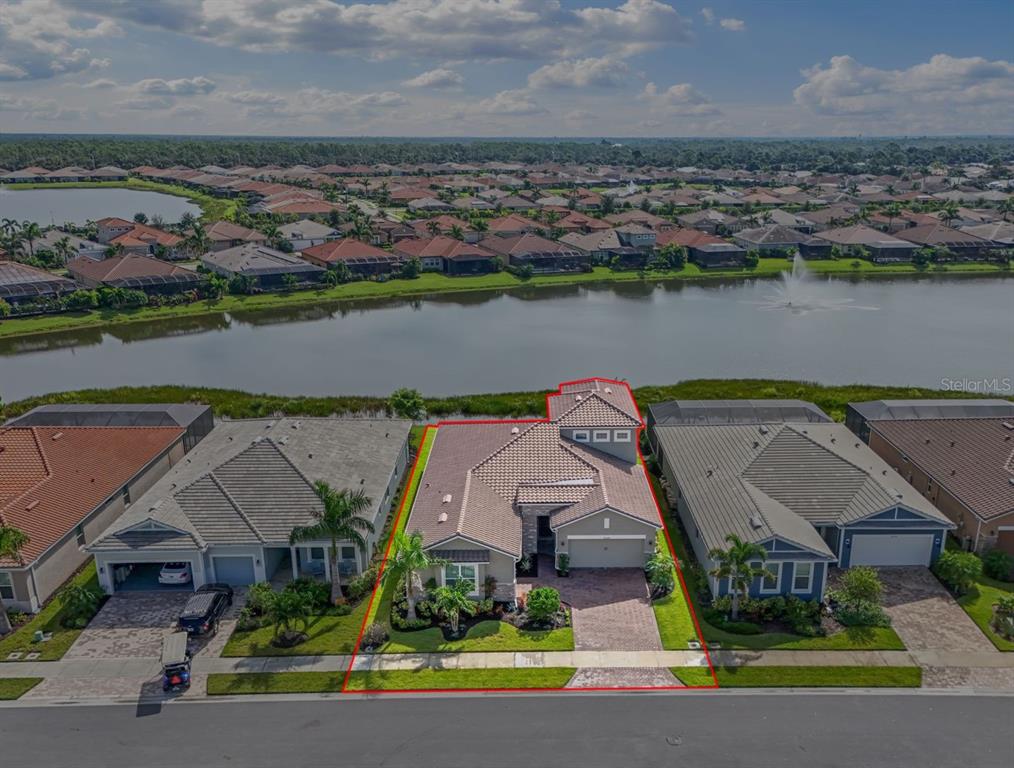 An aerial view shows a single-family home with a tile roof bordering a lake — 20380 SYMPHONY PLACE, VENICE, FL