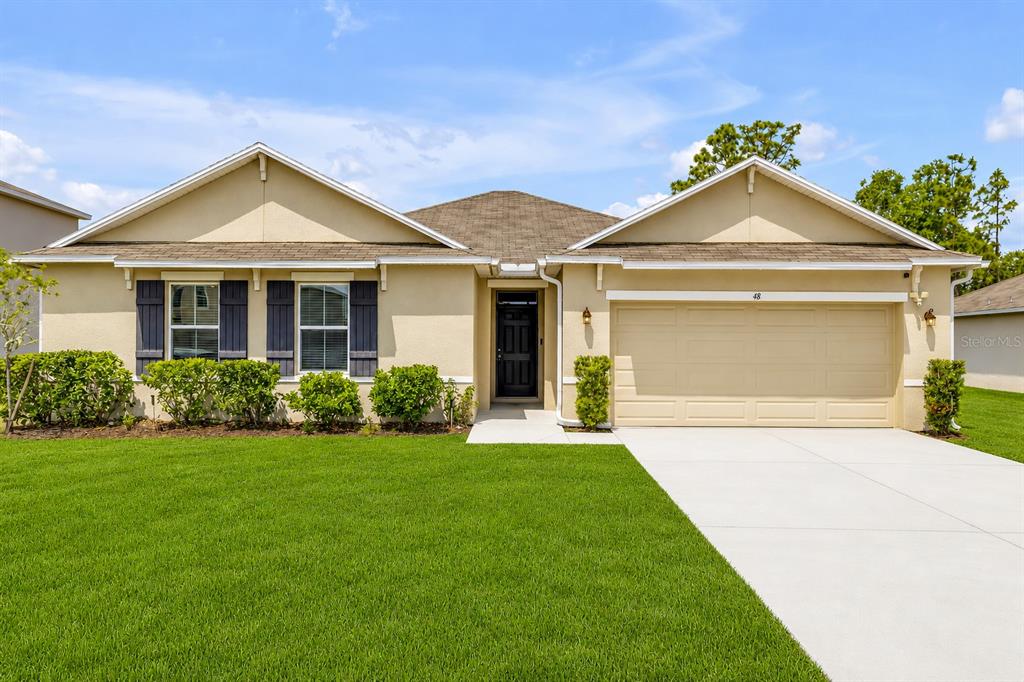 A single-story house with a tan stucco exterior, a two-car garage, and a green lawn — 48 HICKORY COURSE, OCALA, FL