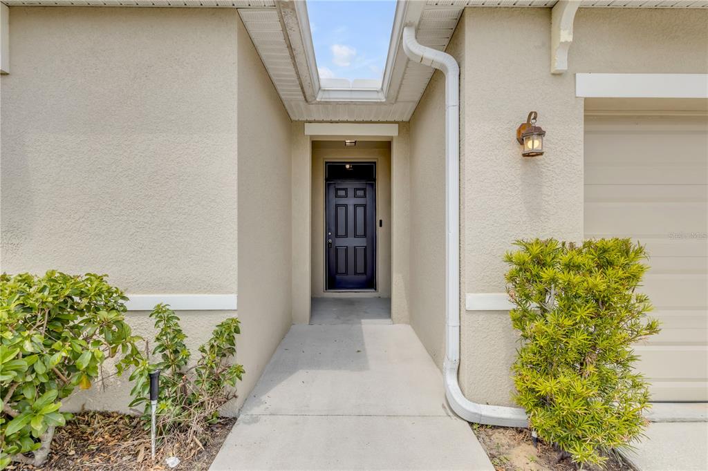 A concrete walkway leads to a dark front door recessed under a covered entryway — 48 HICKORY COURSE, OCALA, FL
