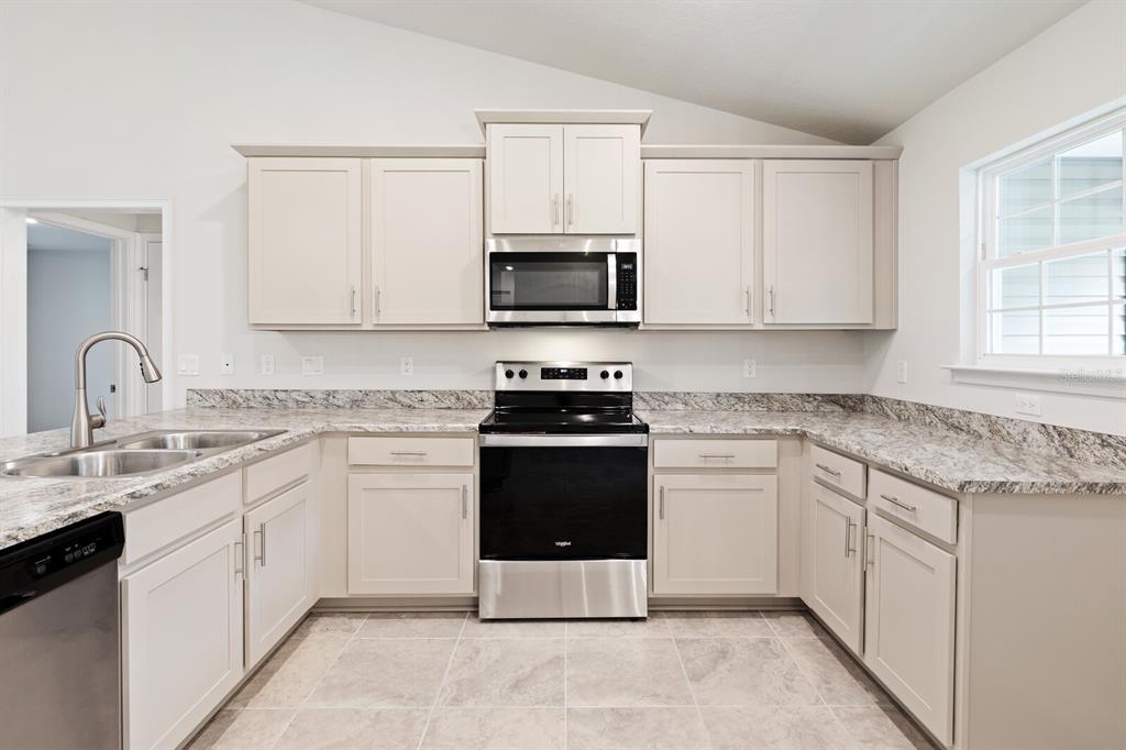 A kitchen features light-colored cabinets, granite countertops, stainless steel appliances, and tile flooring — 9 LAMAR LANE, PALM COAST, FL