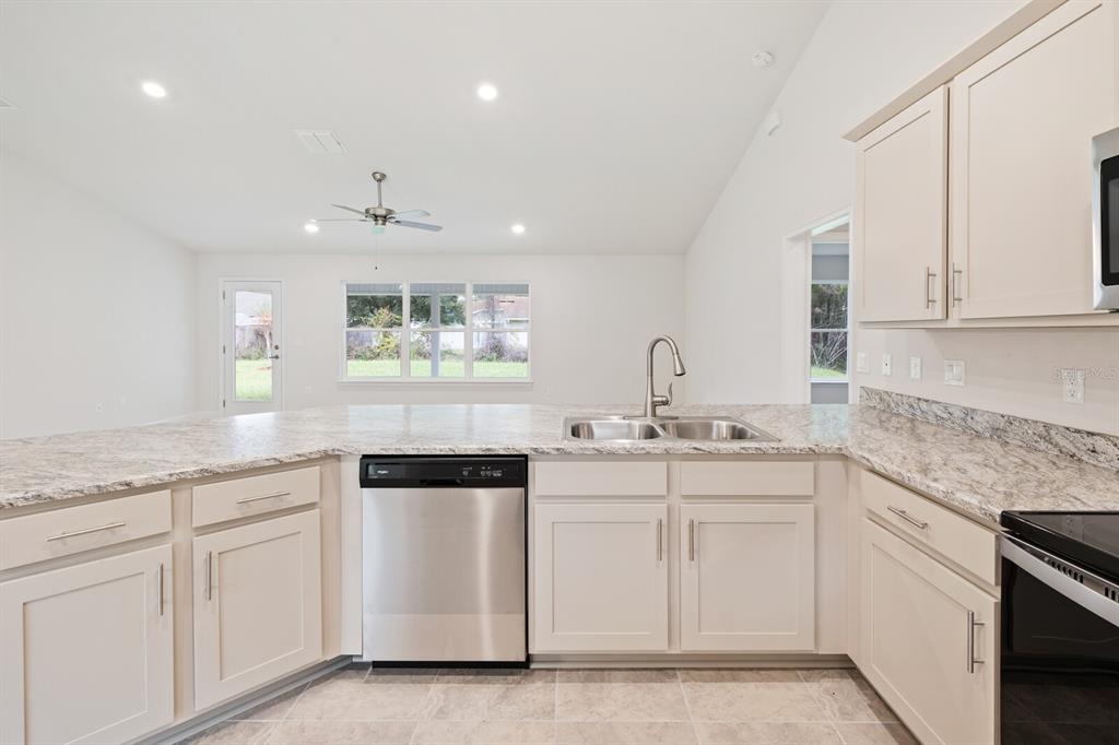A kitchen features light-colored cabinets, granite countertops, stainless steel appliances, and an open floor plan — 9 LAMAR LANE, PALM COAST, FL