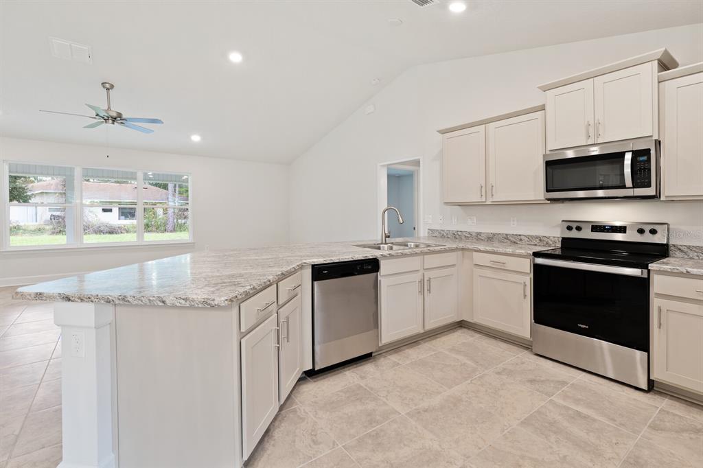 A kitchen with white cabinets, granite countertops, and stainless steel appliances opens to a living area — 9 LAMAR LANE, PALM COAST, FL