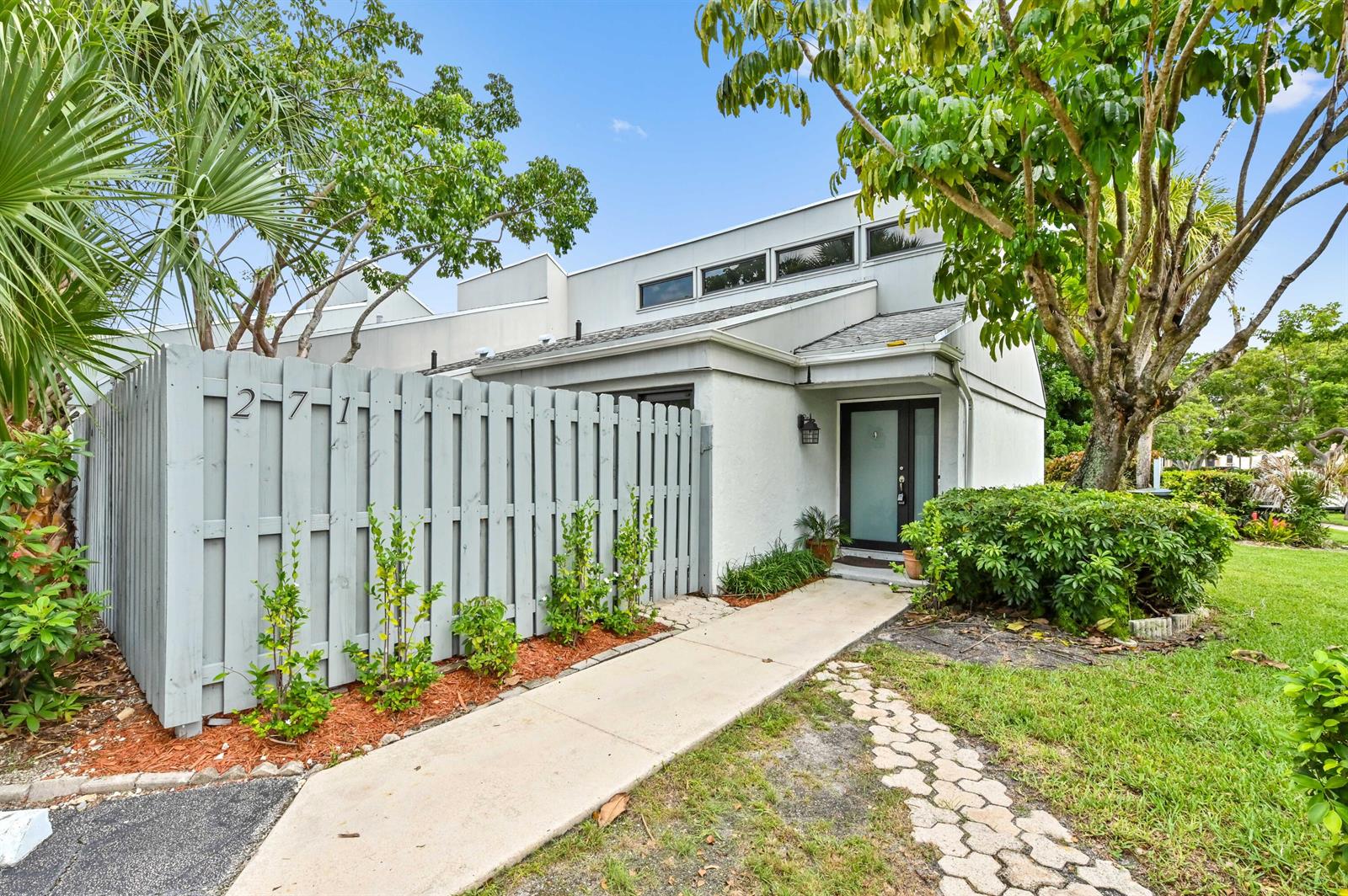 A light gray townhouse exterior features a wooden privacy fence, a concrete walkway, and landscaping — 271 NW 15th Street, Boca Raton FL 33432, BOCA RATON, FL