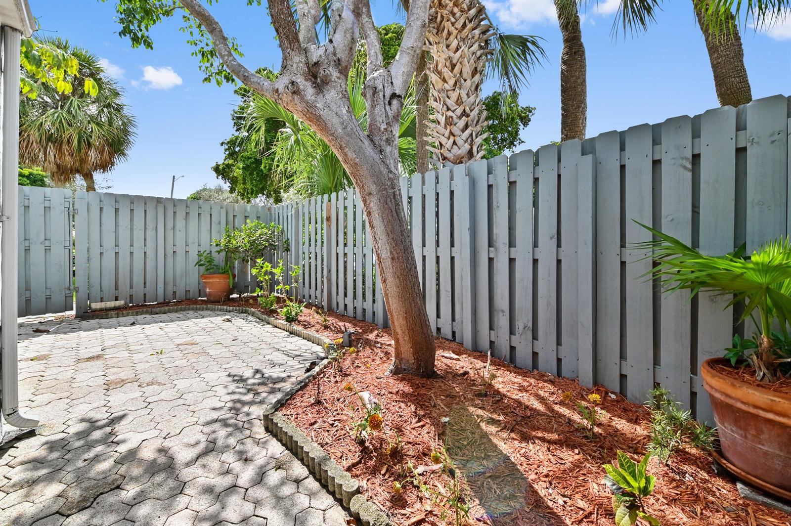 A paved patio area features a tree, mulch beds, and a gray wooden privacy fence — 271 NW 15th Street, Boca Raton FL 33432, BOCA RATON, FL