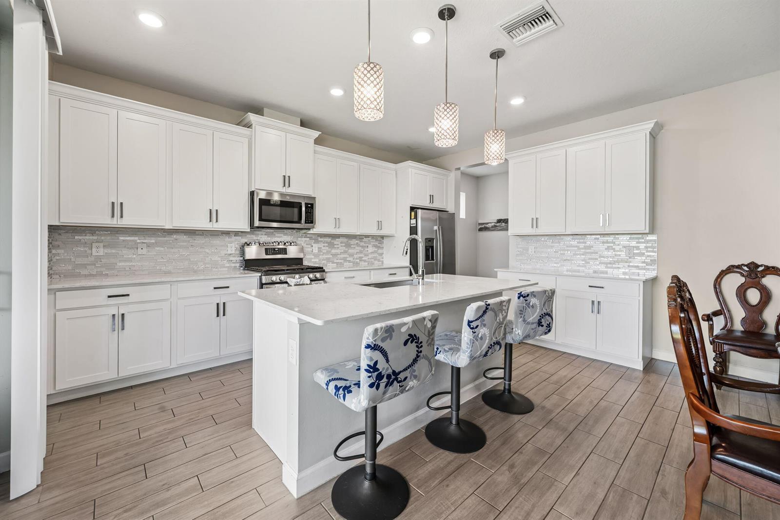 A modern kitchen features white cabinetry, a central island with bar stools, and tiled flooring — 1408 Wandering Willow Way, Loxahatchee FL 33470, LOXAHATCHEE, FL
