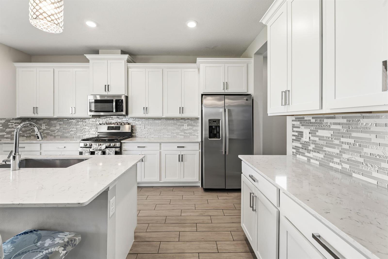 A modern kitchen features white cabinets, stainless steel appliances, quartz countertops, and a tile backsplash — 1408 Wandering Willow Way, Loxahatchee FL 33470, LOXAHATCHEE, FL
