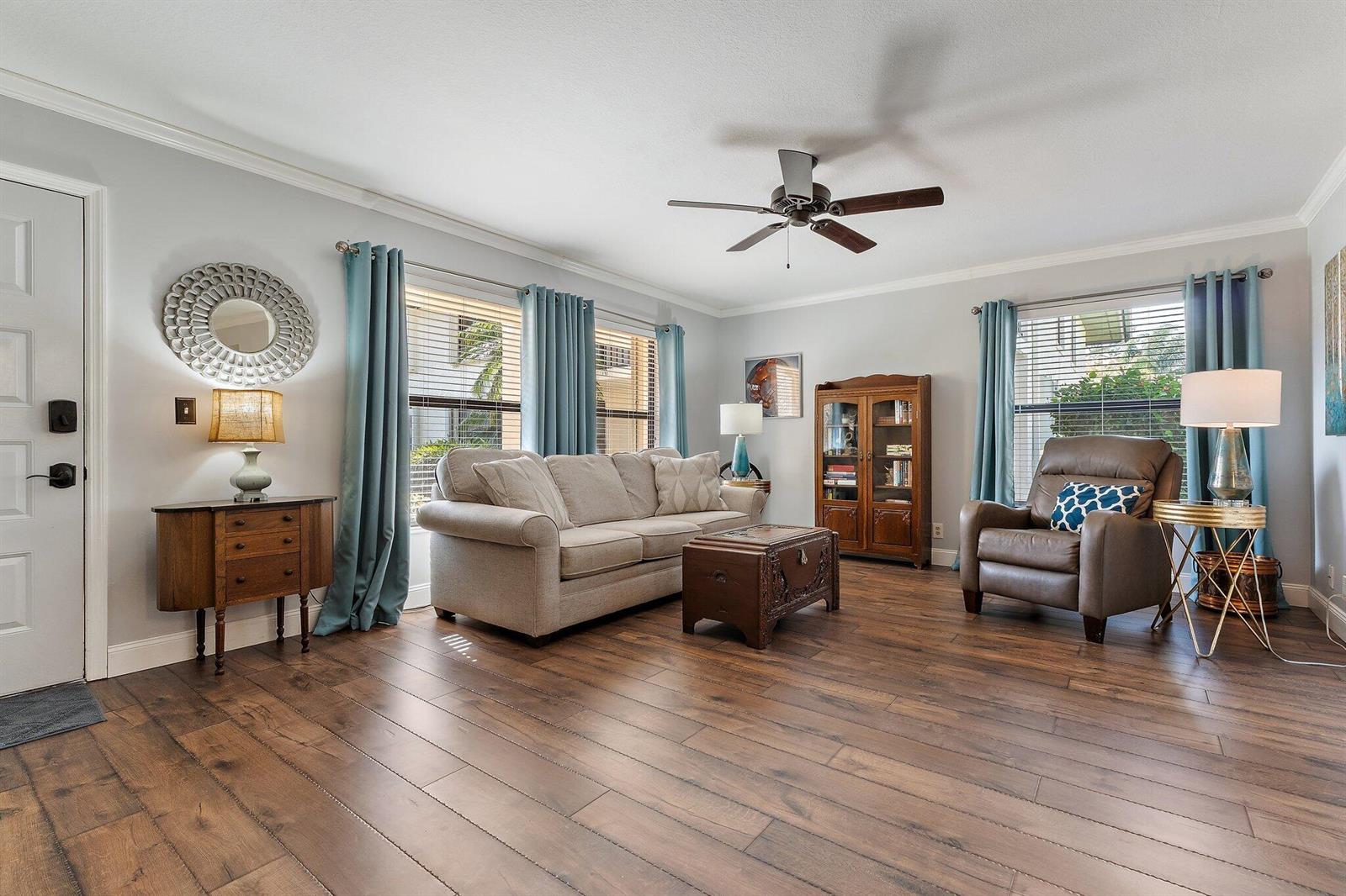 A living room features light gray walls, wood-look flooring, a sofa, and a leather armchair — 671 SW South River Drive # 105, Stuart FL 34997, STUART, FL
