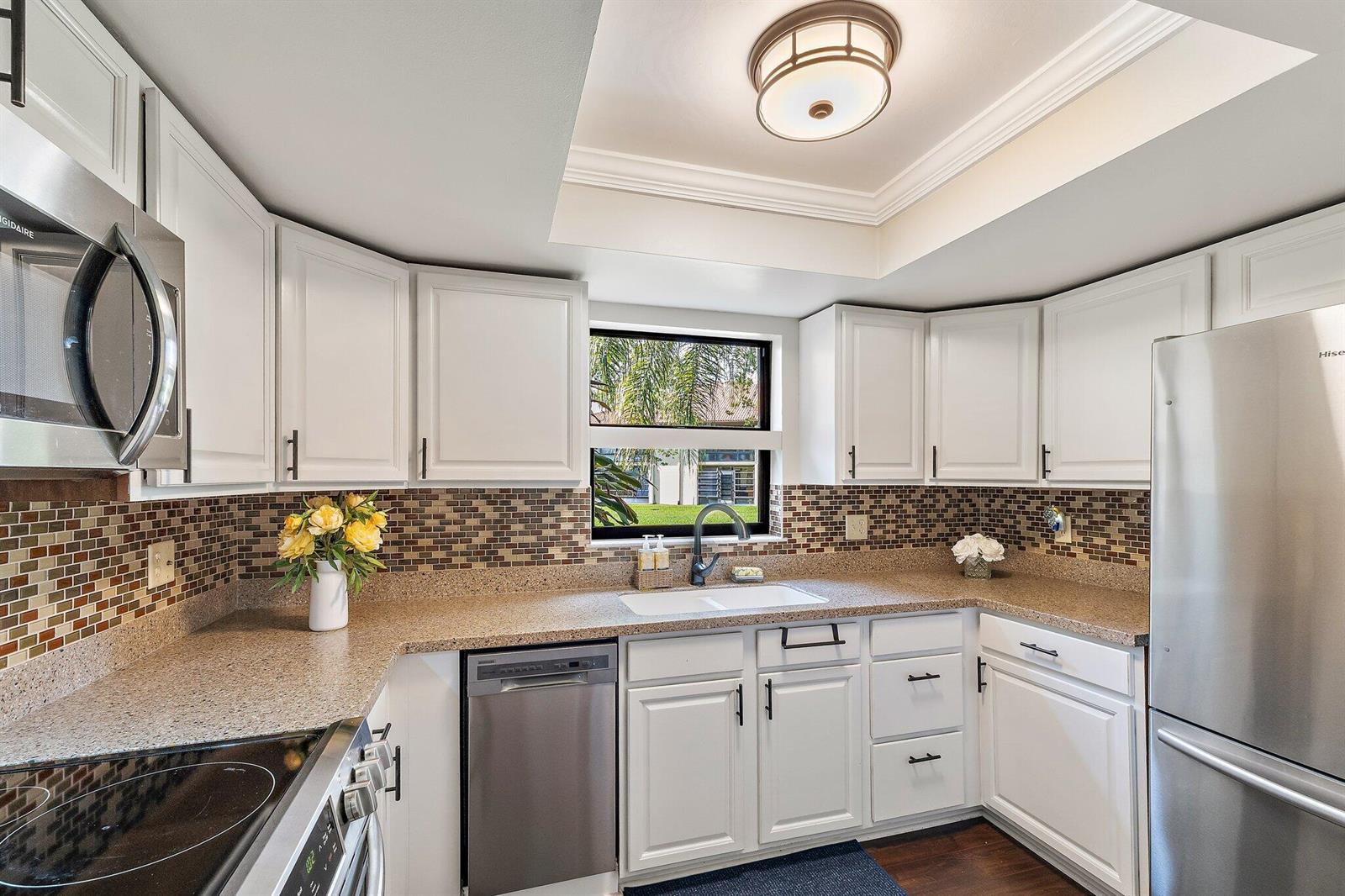 A kitchen with white cabinets, stainless steel appliances, granite countertops, and a mosaic tile backsplash — 671 SW South River Drive # 105, Stuart FL 34997, STUART, FL