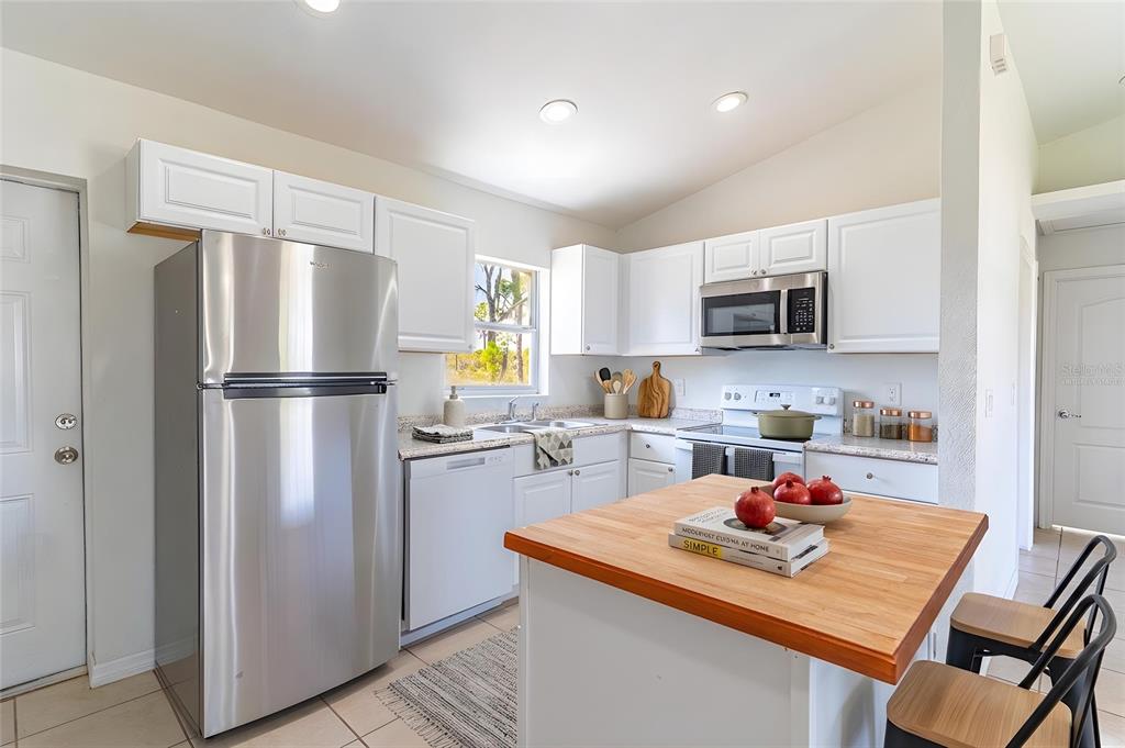 A kitchen features white cabinets, stainless steel appliances, a wooden island, and tile flooring — 1411 BITTERSWEET STREET, LAKE PLACID, FL