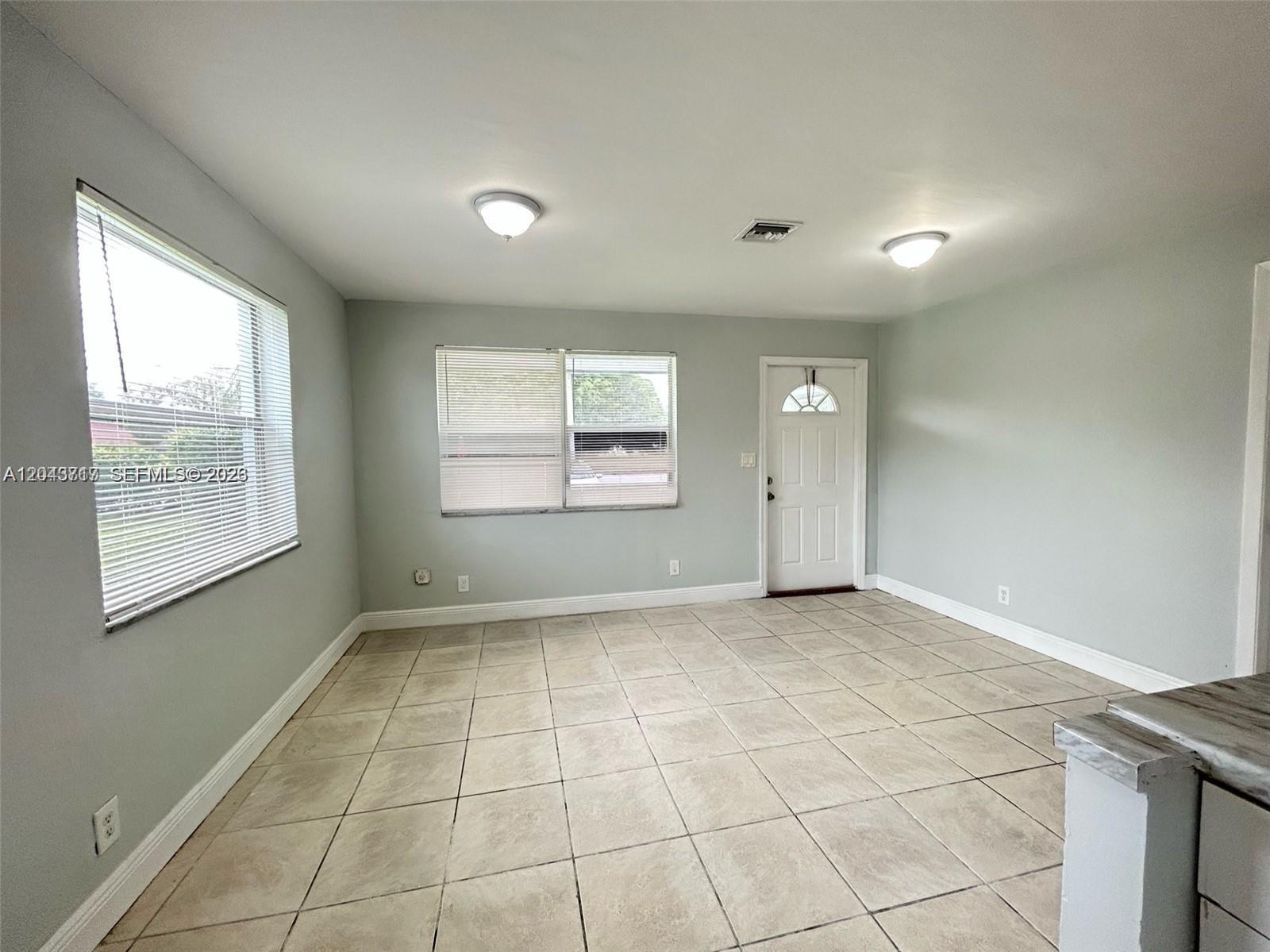 An empty room features light gray walls, tile flooring, two windows with blinds, and a door — 101 NW 13th Ave, Dania Beach FL 33004, DANIA BEACH, FL