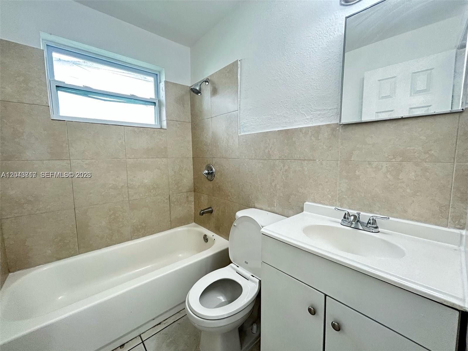 A bathroom features a white vanity, a toilet, and a bathtub with beige wall tiles — 101 NW 13th Ave, Dania Beach FL 33004, DANIA BEACH, FL