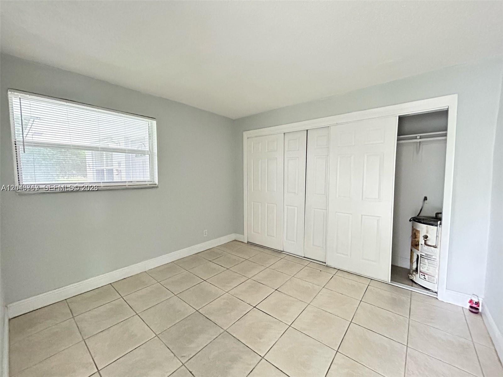 A bedroom with light gray walls, tile flooring, a window with blinds, and a closet — 101 NW 13th Ave, Dania Beach FL 33004, DANIA BEACH, FL