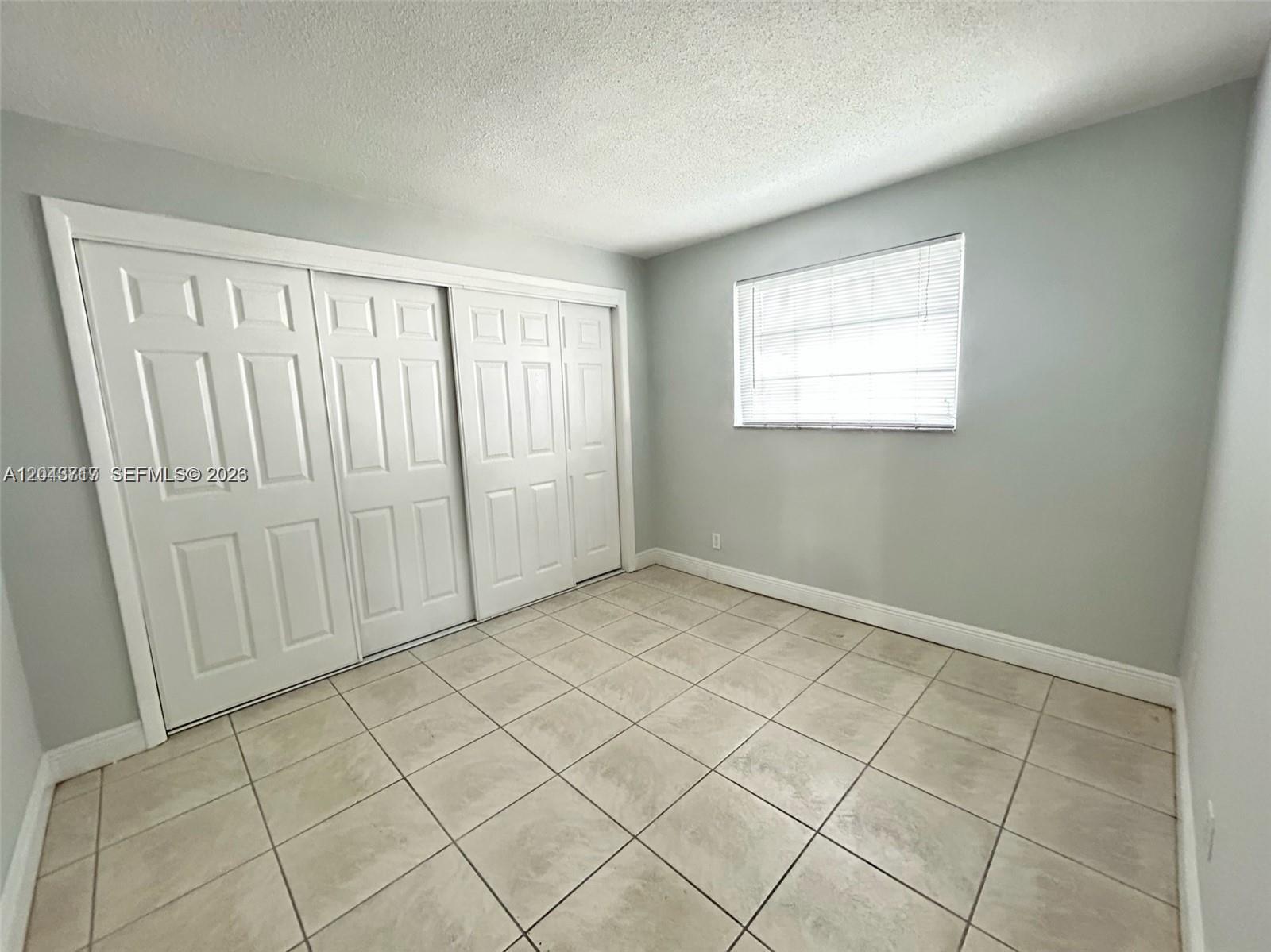 A bedroom features light gray walls, white sliding closet doors, and beige tiled flooring — 101 NW 13th Ave, Dania Beach FL 33004, DANIA BEACH, FL