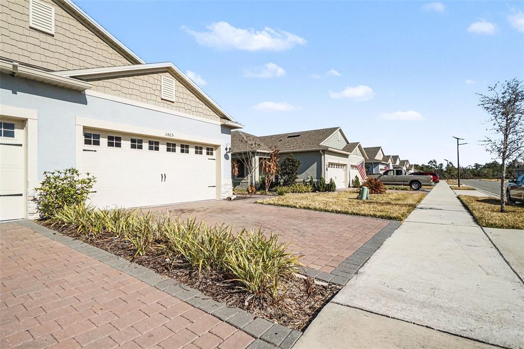 A residential street view showing a house with a brick driveway and a garage — 3465 MEADOW BEAUTY WAY, CLERMONT, FL