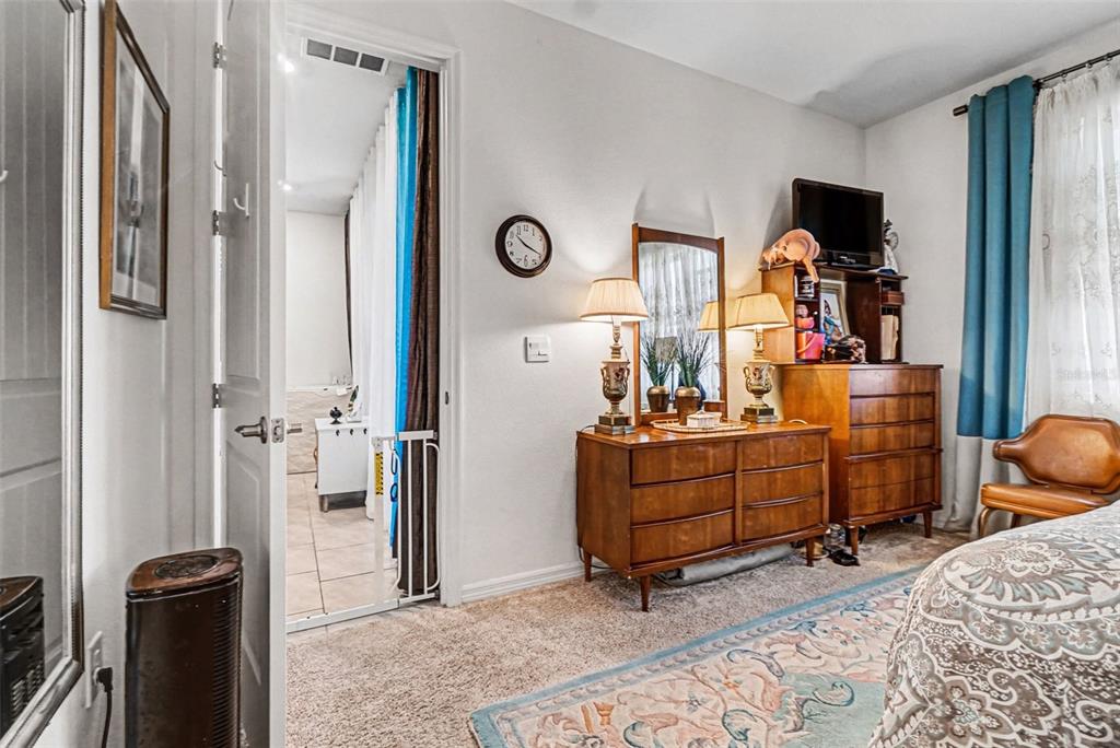 A bedroom features a wooden dresser, a wall clock, and a doorway leading to a bathroom — 3465 MEADOW BEAUTY WAY, CLERMONT, FL