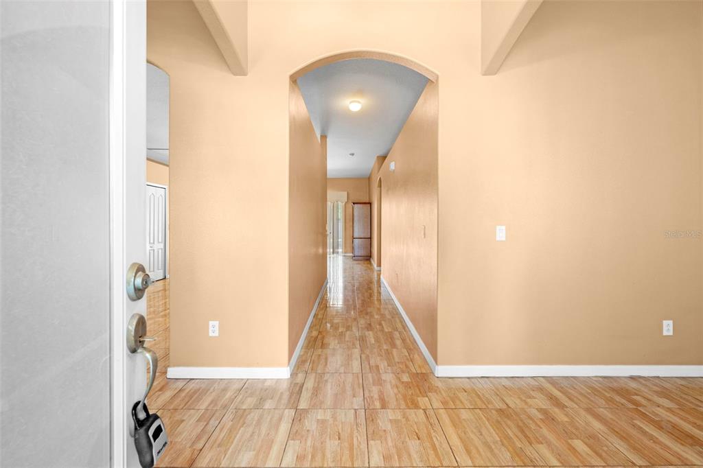 A hallway with light-colored walls and wood-look tile flooring leads toward a distant doorway — 4211 BLAKEMORE PLACE, SPRING HILL, FL