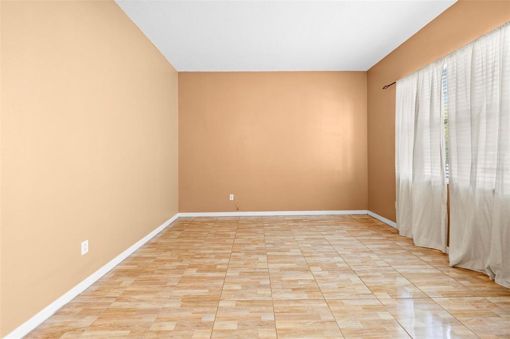 An empty room with tan walls, tiled flooring, and white curtains covering a large window — 4211 BLAKEMORE PLACE, SPRING HILL, FL