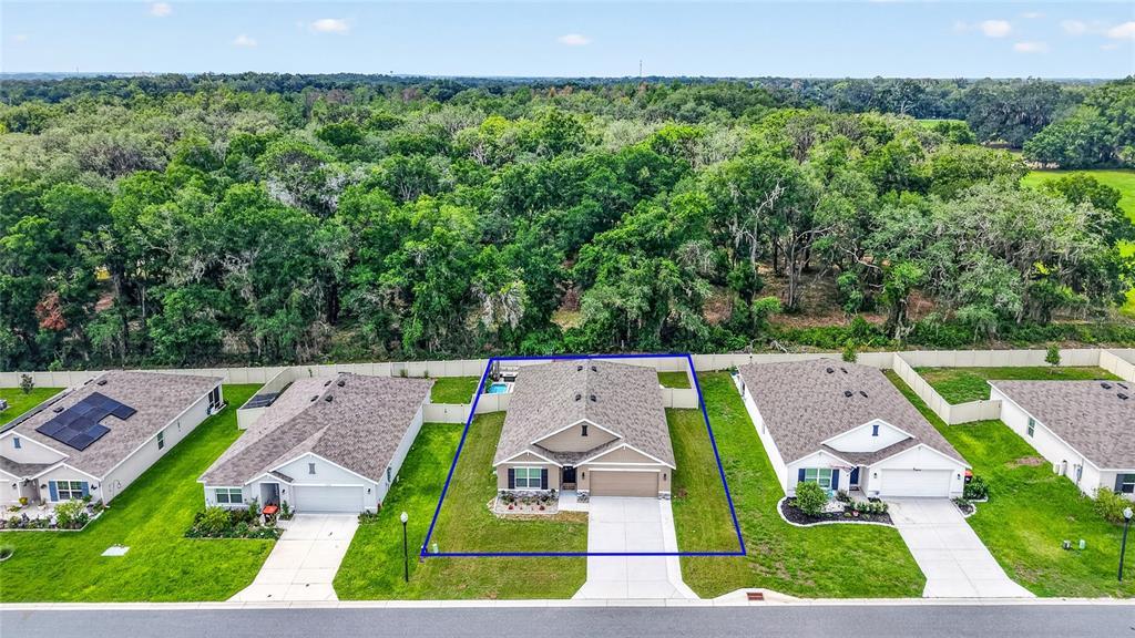An aerial view shows a suburban house with a fenced backyard bordering a dense forest — 10342 SE 162ND PLACE ROAD, SUMMERFIELD, FL