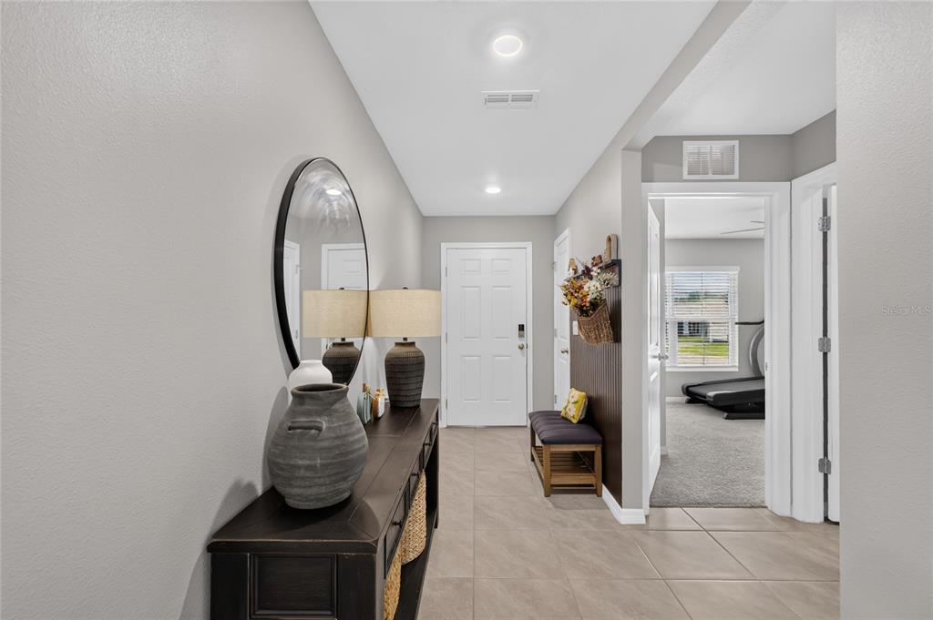 A tiled entryway features a dark wood console table, a round mirror, and a bench — 10342 SE 162ND PLACE ROAD, SUMMERFIELD, FL