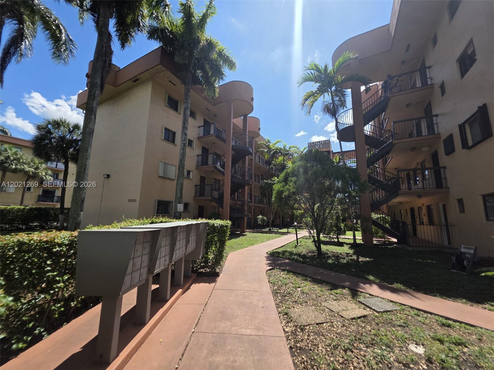 An outdoor walkway leads between two multi-story apartment buildings with external staircases and palm trees — 5560 W 21st Ct # 308, Hialeah FL 33016, HIALEAH, FL