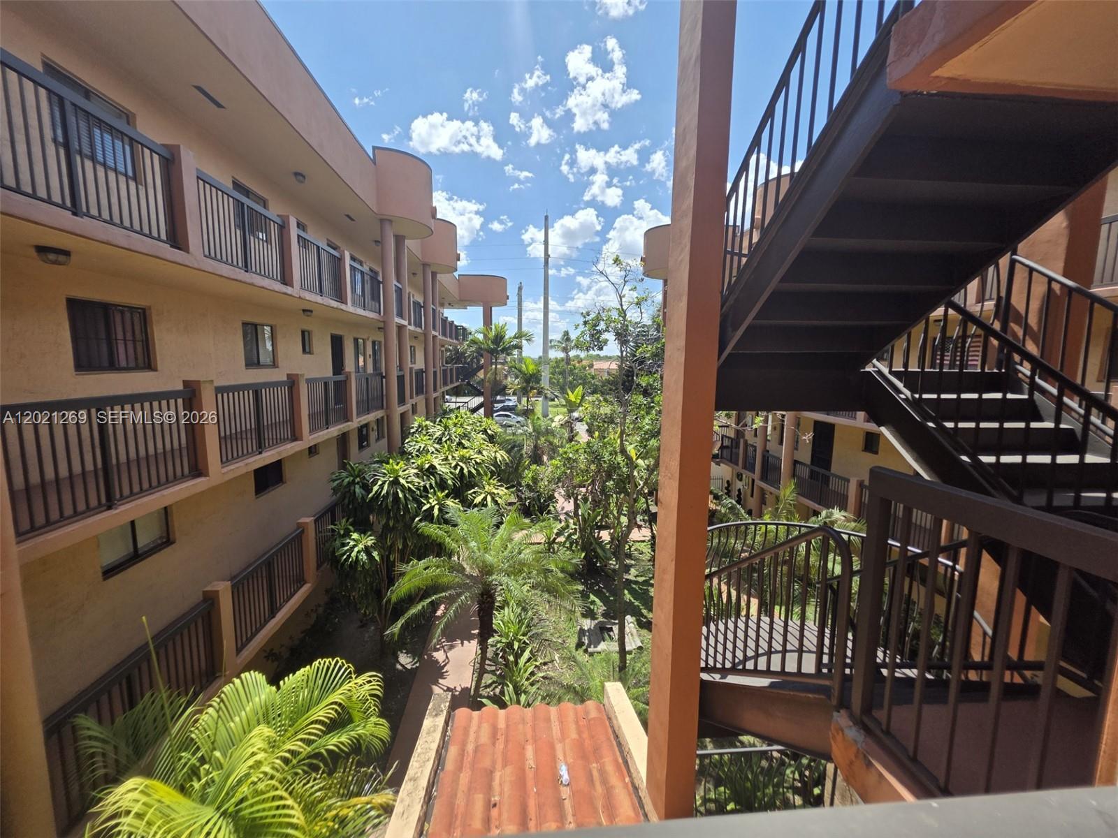 An outdoor view of a multi-story apartment complex with balconies, staircases, and tropical landscaping — 5560 W 21st Ct # 308, Hialeah FL 33016, HIALEAH, FL