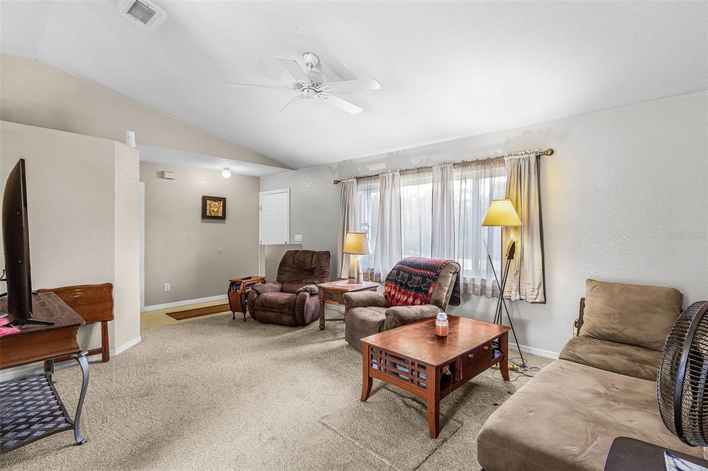 A living room features beige carpeting, a vaulted ceiling, a ceiling fan, and brown furniture — 27491 LAS LOMAS DRIVE, PUNTA GORDA, FL
