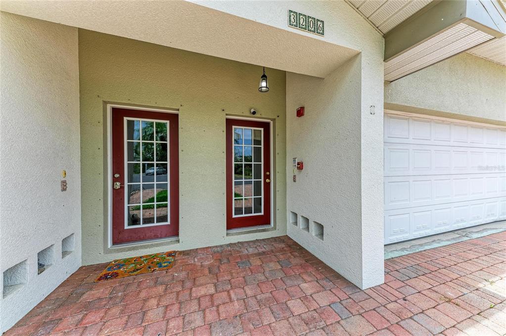 A brick-paved entryway features two red glass-paneled doors and an adjacent white garage door — 3206 10TH LN W, PALMETTO, FL