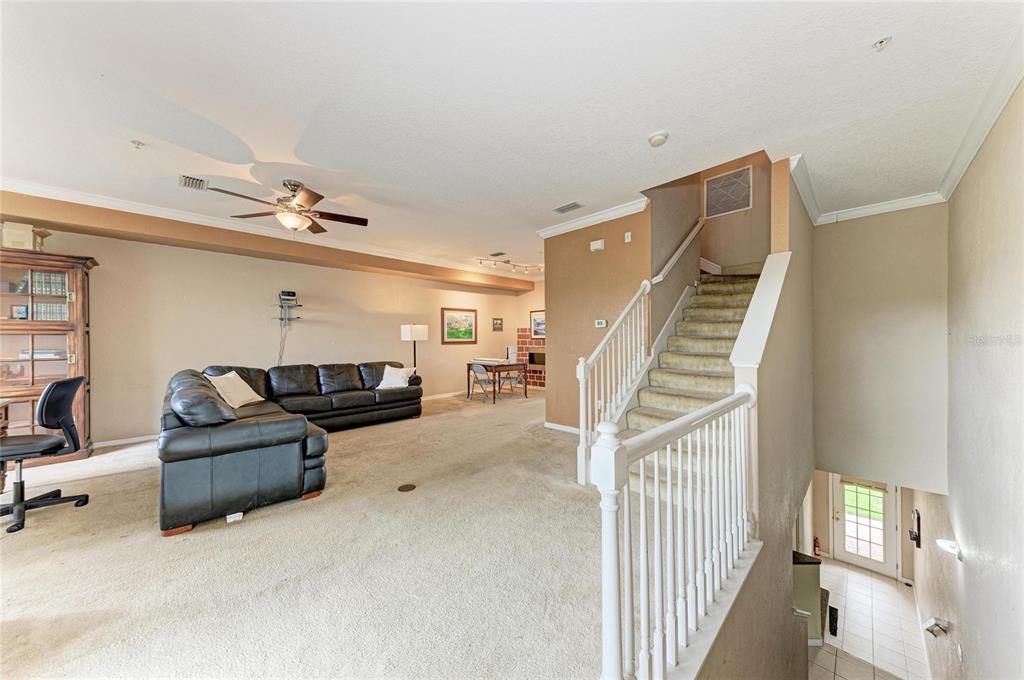 A carpeted living room features a black sectional sofa, a staircase, and a ceiling fan — 3206 10TH LN W, PALMETTO, FL