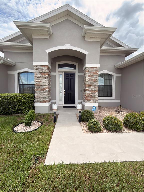 The exterior of a gray house features a stone-accented entryway and a black front door — 4086 DINNER LAKE WAY, LAKE WALES, FL