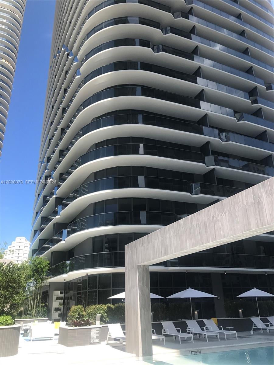 A low-angle view shows a modern high-rise building with curved balconies overlooking a swimming pool — 55 SW 9th St # 1607, Miami FL 33130, MIAMI, FL