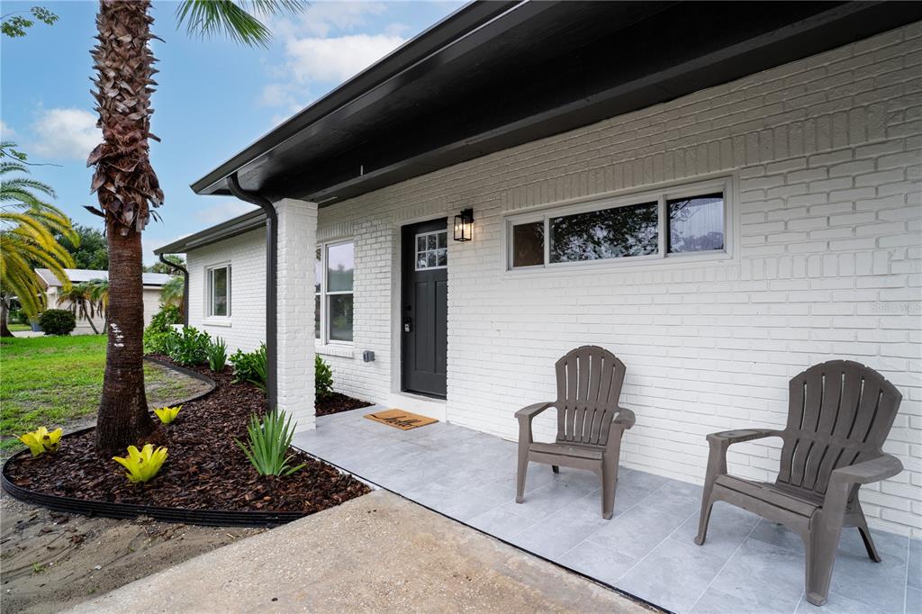 A white brick house exterior features a gray front door, tiled porch, and two chairs — 11309 115TH STREET, LARGO, FL