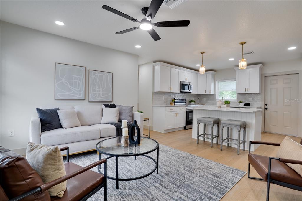 An open-concept living room and kitchen featuring white cabinetry, a kitchen island, and hardwood floors — 11309 115TH STREET, LARGO, FL