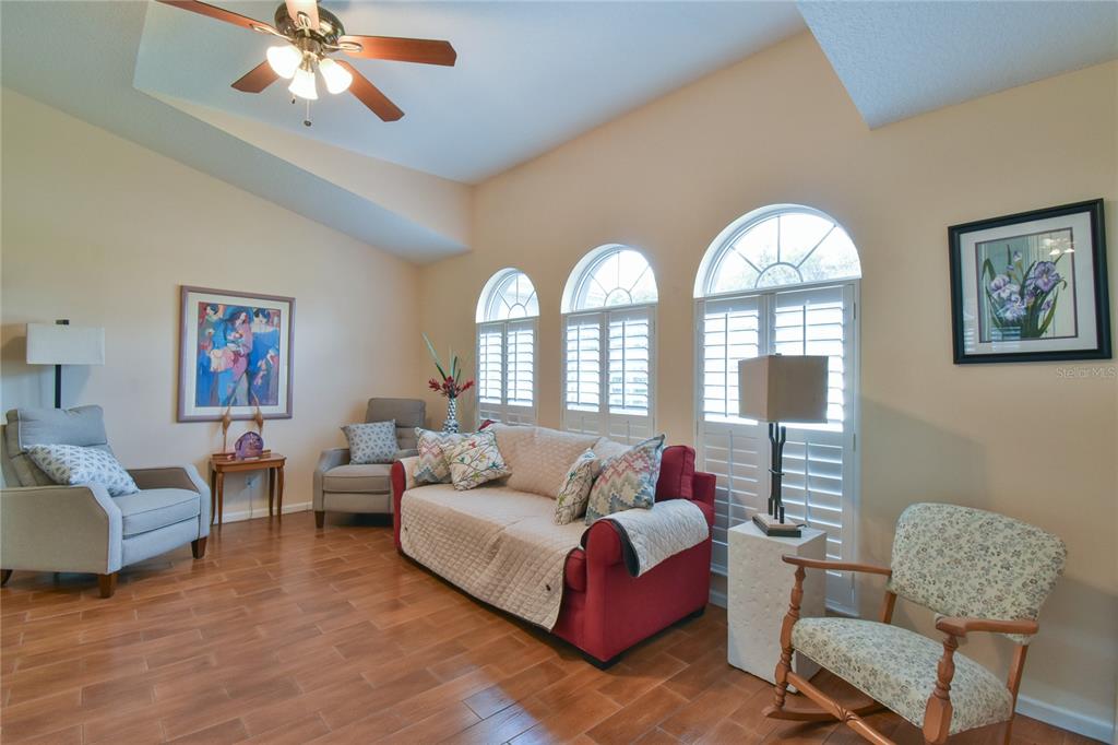 A living room features a red sofa, several armchairs, arched windows, and wood-look tile flooring — 4993 NW 18TH STREET, OCALA, FL