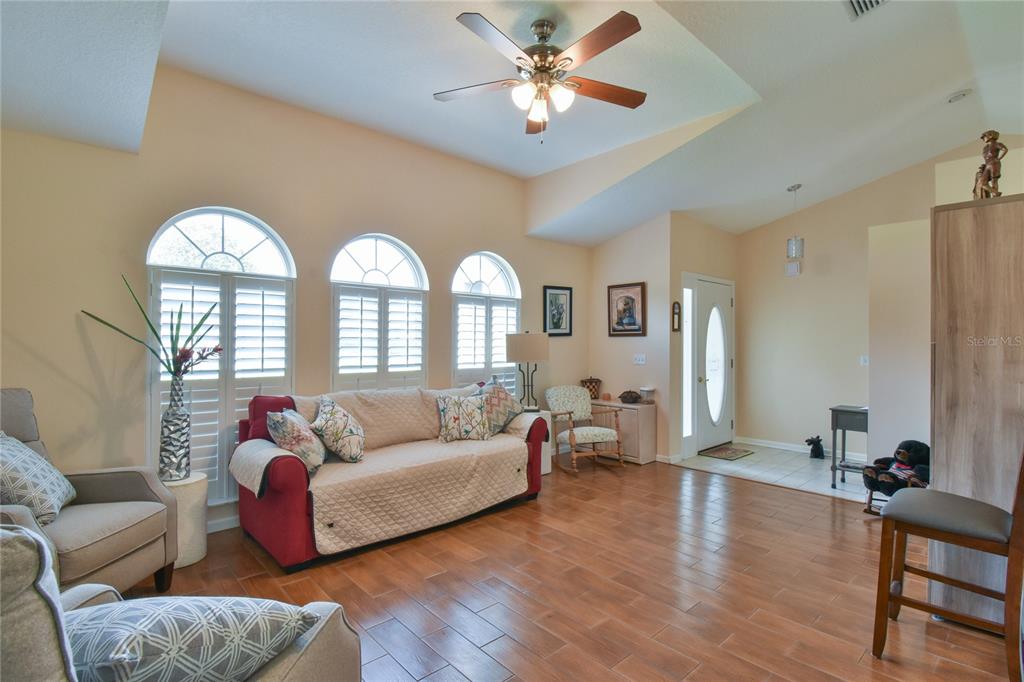 A living room with wood-look tile flooring, a ceiling fan, and three arched windows — 4993 NW 18TH STREET, OCALA, FL