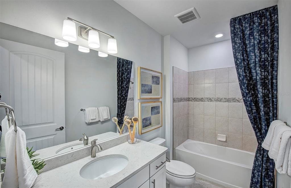 A bathroom features a white vanity with a quartz countertop, a mirror, and a tub-shower — 4739 BLUE STAR COURT, NORTH PORT, FL