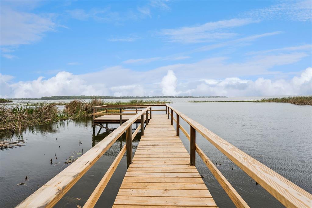 A wooden dock with railings extends over a lake toward a distant shoreline — 2316 N GRIFFIN DRIVE, LEESBURG, FL