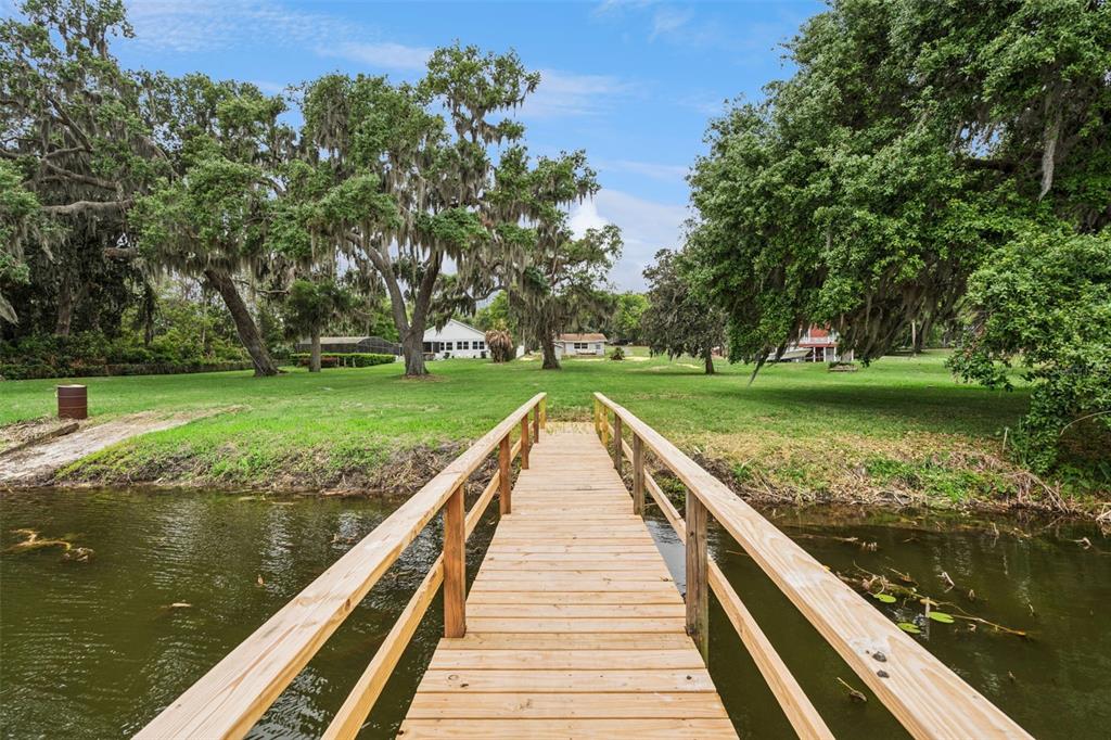 A wooden dock extends over a lake toward a grassy yard with large oak trees — 2316 N GRIFFIN DRIVE, LEESBURG, FL