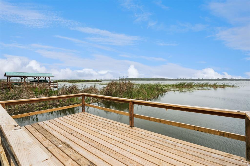 A wooden deck with railings overlooks a lake with a boat dock and tall grasses — 2316 N GRIFFIN DRIVE, LEESBURG, FL