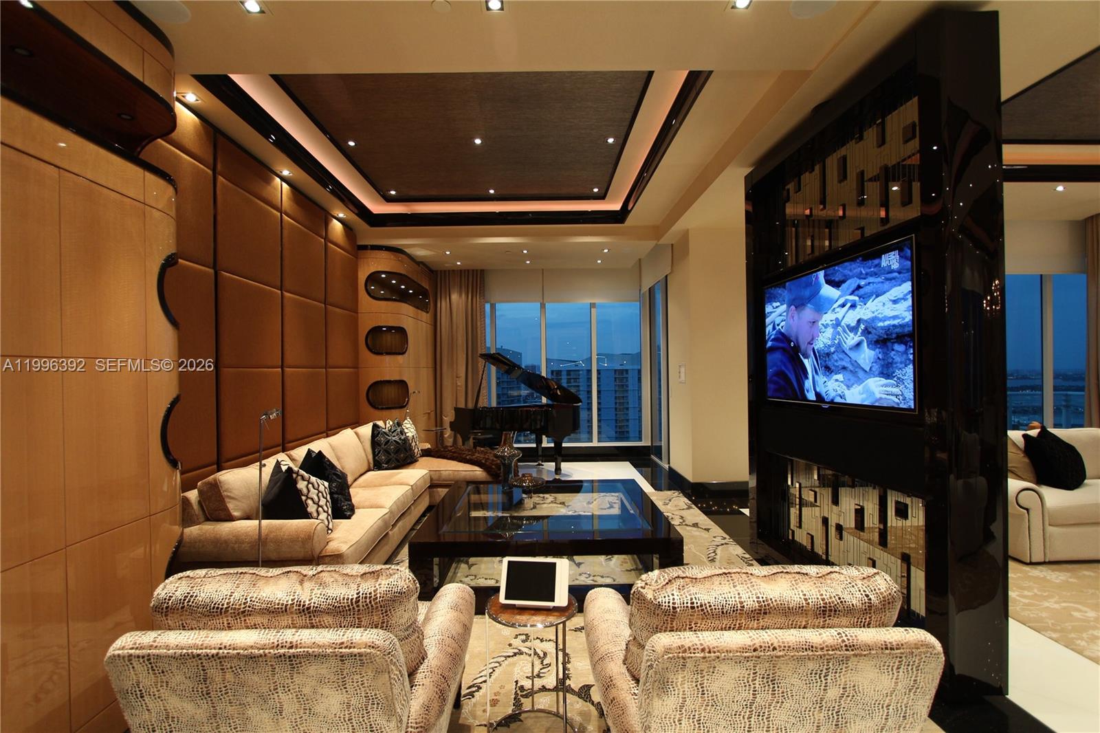 A modern living room features a grand piano, a large television, and textured wall panels — 900 Brickell Key Blvd, Miami FL 33131, MIAMI, FL