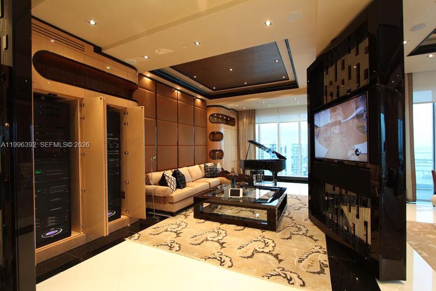 A modern living room features a grand piano, a large television, and built-in equipment racks — 900 Brickell Key Blvd, Miami FL 33131, MIAMI, FL