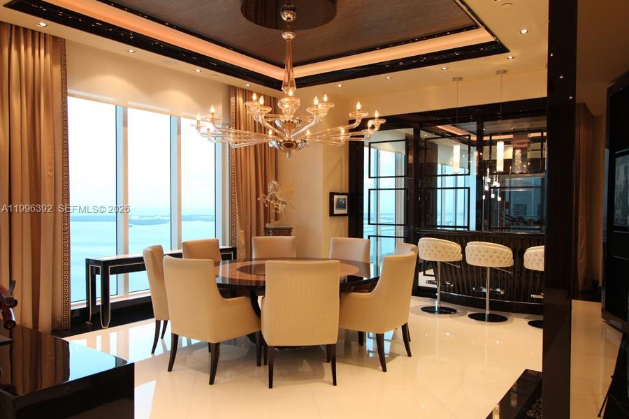 A dining room features a round table, upholstered chairs, a crystal chandelier, and floor-to-ceiling windows — 900 Brickell Key Blvd, Miami FL 33131, MIAMI, FL