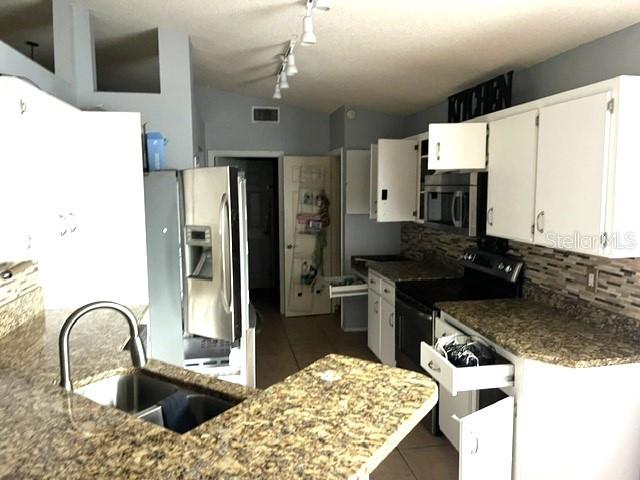 A kitchen features granite countertops, white cabinetry, stainless steel appliances, and a double-basin sink — 26 SAINT KITTS CIRCLE, WINTER HAVEN, FL