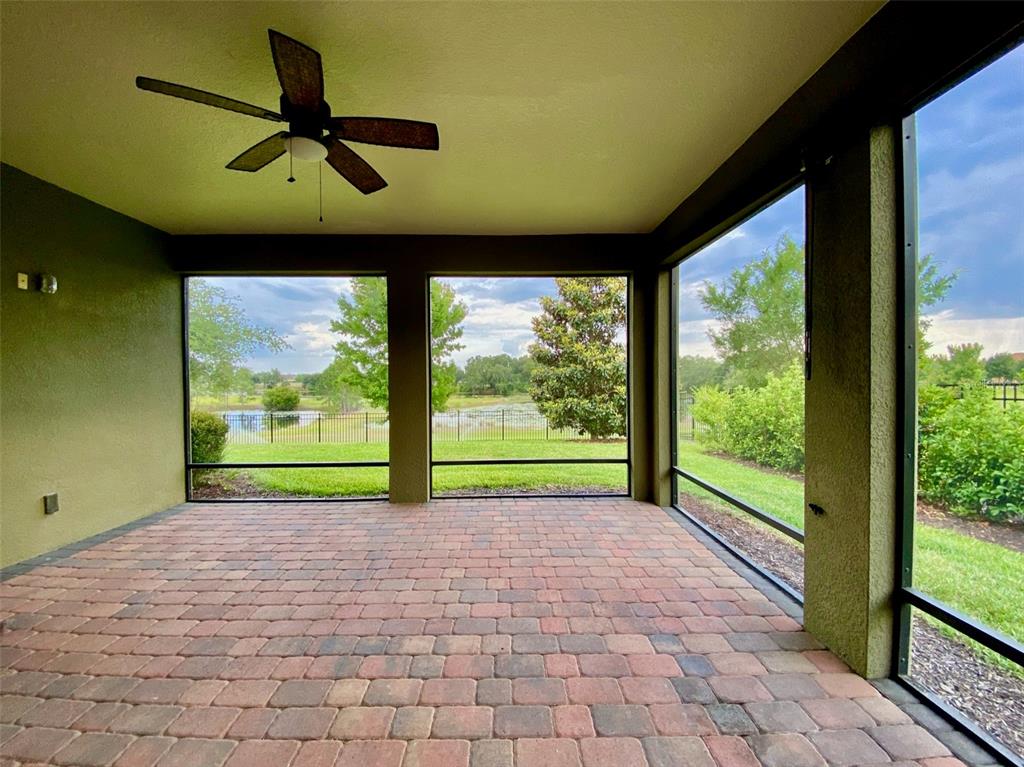 A covered patio with brick pavers, a ceiling fan, and screened walls overlooking a pond — 16238 WIND VIEW LANE, WINTER GARDEN, FL