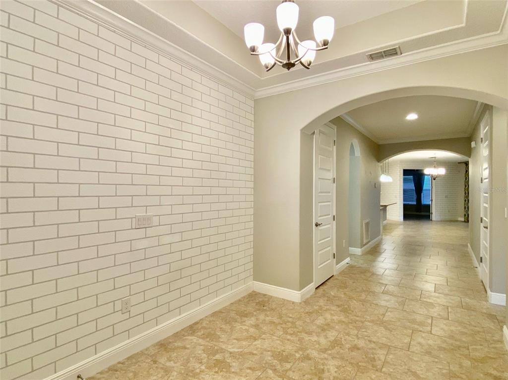 A room with a white brick accent wall, tile flooring, and a chandelier — 16238 WIND VIEW LANE, WINTER GARDEN, FL