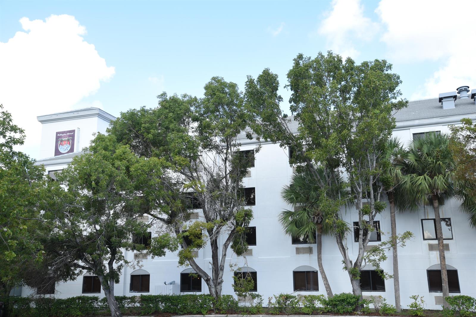 A multi-story white building with dark windows is partially obscured by several large green trees — 7051 N Seacrest Boulevard, Lantana FL 33462, LANTANA, FL